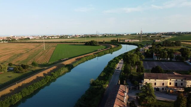 Drone shot of a serene countryside scene featuring a winding river bordered by lush greenery and fields in Caorle Italy