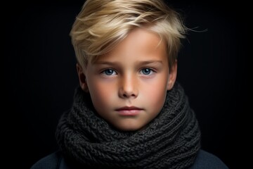 Portrait of a cute little boy with blond hair and blue eyes wearing a scarf. Studio shot.