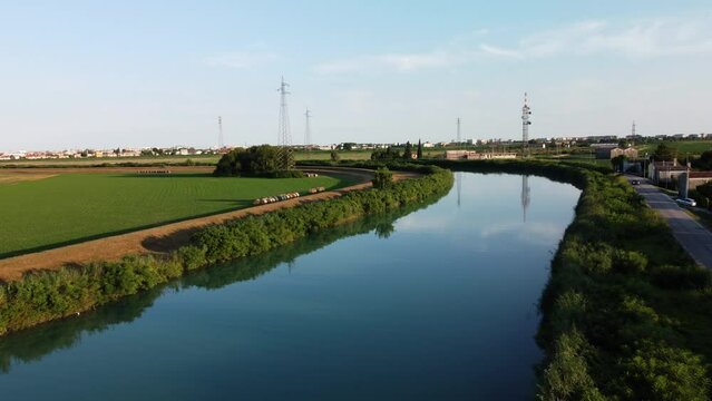 Drone shot flying above a winding river bordered by lush greenery and fields in Caorle Italy