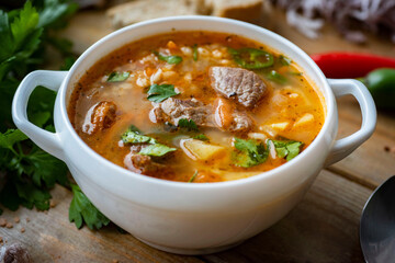Spicy soup with vegetables and beef in a white plate on a wooden table for lunch. Close-up
