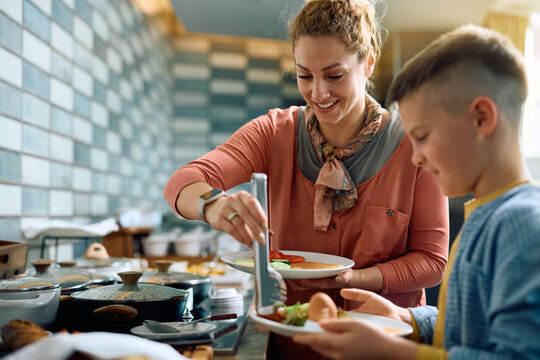 Happy mother with son eating breakfast at hotel restaurant.