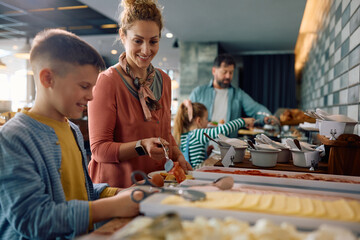 Happy woman and her family enjoying in buffet breakfast at hotel restaurant.
