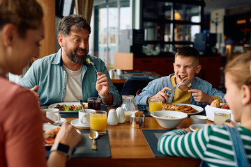 Happy father talking to his family while eating breakfast in hotel.