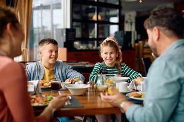 Happy kids talking to their parents while having breakfast in hotel restaurant.