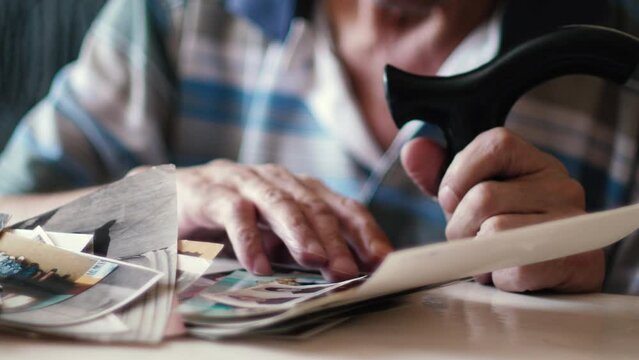 an old man remembers the past. a pensioner sitting with a walking cane and his old photographs. a pensioner and his archive of family photographs