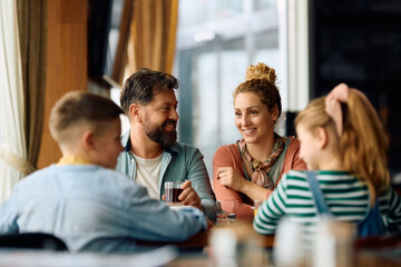 Happy family talking while eating at dining table in restaurant. - obrazy, fototapety, plakaty