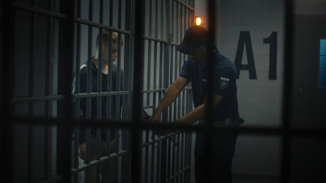 Warden takes off handcuffs from young prisoner. Teenager serves imprisonment term in correctional facility or detention center. Young inmate in prison cell. Justice system. View through metal bars.