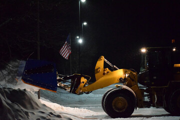 Blue Payloader Snow Pusher Stacking Snowbanks In Front of An American Flag