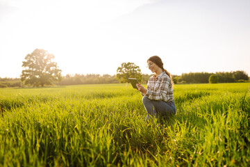 Woman Farmer on a green wheat field with a tablet in his hands. Smart farm. The concept of the...