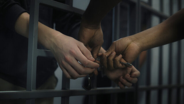 Warden takes off handcuffs from young prisoner. Multi ethnic teenagers serve imprisonment term in correctional facility or detention center. Young inmates in prison cell. Justice system. Close up.