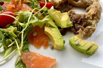 On a white plate - a salad of tomatoes, green arugula, avocado, salmon and mushrooms
