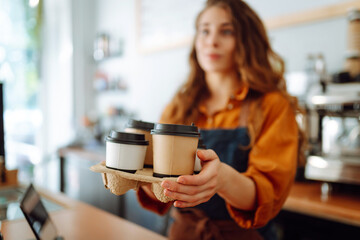 Portrait of a young woman barista holding takeaway coffee in her hands. Takeaway food. Business...