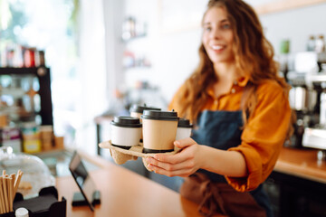 Portrait of a young woman barista holding takeaway coffee in her hands. Takeaway food. Business concept.