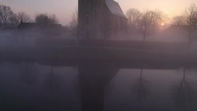 Aerial view of church (Kerk van Hichtum) in small town during foggy sunrise, Hichtum, Netherlands