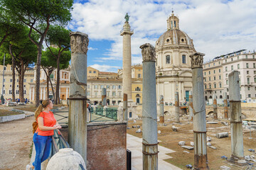 A woman tourist looks at Roman Imperial Forums with Chiesa del Santissimo Nome di Maria al Foro Traiano church in the background.