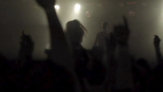 Two beautiful young women DJ play the music on the mixing console in the nightclub. Against the background of unrecognizable people. Slow motion