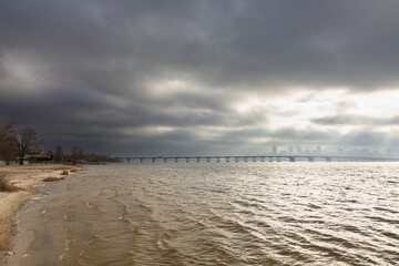 Dnipro River, Dnipro city, Ukraine. Cityscape with sky with clouds and river and city bridge. Cloudy clouds hang over and the sun's rays shine on the cityscape.