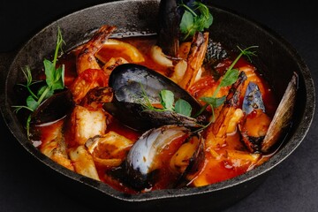 Delicious seafood skillet with flavorful tomato broth and fresh herbs on elegant black background