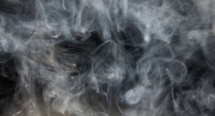 White puffs of smoke, steam or fog on dark background.