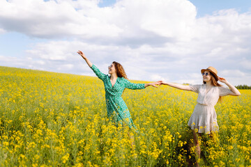 Naklejka na ściany i meble Two young women in a beautiful field with yellow flowers. They jump and have fun. Friendship Day