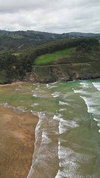 Aerial view of the rugged coastline with greenery and waves, Playa de la Arena, Bilbao, Biscay, Spain.