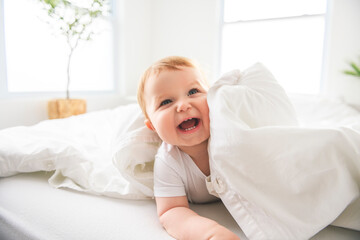 Baby boy in white sunny bedroom. one years child relaxing in bed.