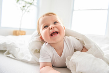 Baby boy in white sunny bedroom. one years child relaxing in bed. - obrazy, fototapety, plakaty