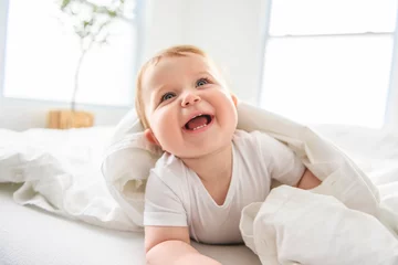 Fototapeten Baby boy in white sunny bedroom. one years child relaxing in bed. © Louis-Photo 
