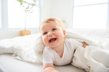 Baby boy in white sunny bedroom. one years child relaxing in bed.