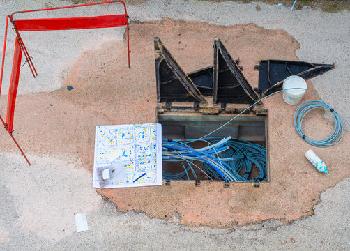 Worker made a break-in with an electric demolition hammer in the reinforced concrete shaft of the fiber optic cable line. Open triangular cast iron manhole covers