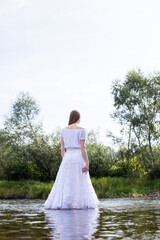 Fototapeta na wymiar Graceful figure of a girl. A woman in a white dress in the water. Woman's wet dress. Bathe in the river