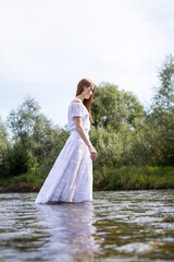 Fototapeta na wymiar Graceful figure of a girl. A woman in a white dress in the water. Woman's wet dress. Bathe in the river