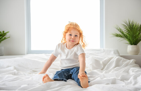 Redhead girl on the bed rests and plays. Cute little girl