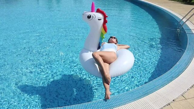 young beautiful woman in swimsuit on inflatable unicorn pool float in pool in the hotel.