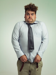 Man, portrait and shocked with plus size pants or big waist in obesity, overweight or measurement on a studio background. Young male person struggling to fit clothing with body fat or chubby stomach - obrazy, fototapety, plakaty