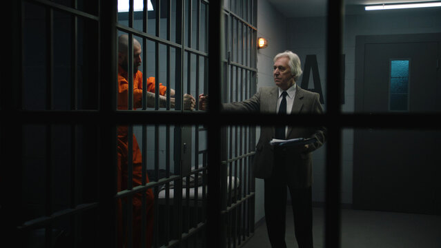 Criminal in orange uniform leans on prison cell bars, talks with advocate and reads lawyer contract. Inmate serves imprisonment term for crime in correctional facility. Gangster in detention center.