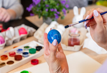 Middle-aged left-handed woman paints Easter eggs with a brush and paints