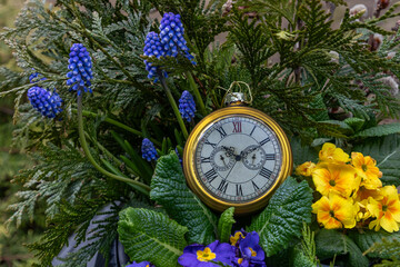 Vintage clock in a bouquet of spring flowers, symbolizing the arrival of spring.