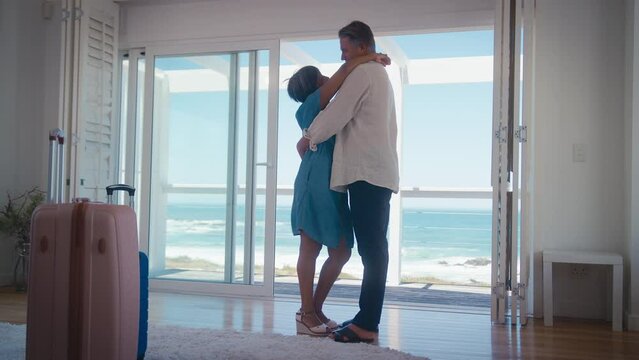 Low angle shot of mature couple with luggage arriving for holiday in beach front property overlooking ocean -  shot in slow motion