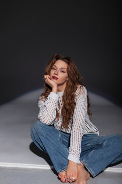 Fashionable beautiful young woman in a fashion white sweater with vintage jeans sits on the floor in the studio