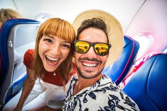 Happy tourist taking selfie inside airplane - Cheerful couple on summer vacation - Passengers boarding on plane - Holidays and transportation concept