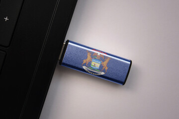 usb flash drive in notebook computer with the national flag of michigan state on gray background.