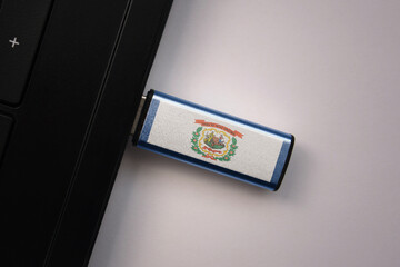 usb flash drive in notebook computer with the national flag of west virginia state on gray background.