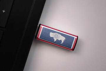 usb flash drive in notebook computer with the national flag of wyoming state on gray background.