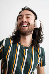 young latin man with braces smiling while listening to music or a podcast with wireless headset...