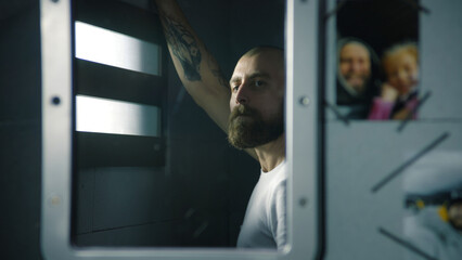 Reflection of male prisoner in mirror looking out the window in prison cell. Photos of family hang...