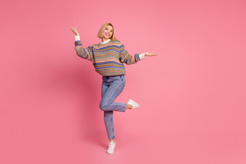 Full size photo of gorgeous girl wear ornament sweater jeans dancing palm hold object empty space isolated on pink color background
