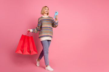 Full size photo of attractive girl hold shopping bags read order taxi on smartphone go empty space isolated on pink color background