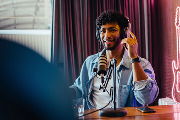 Happy young man hosting podcast show with headphones in modern studio