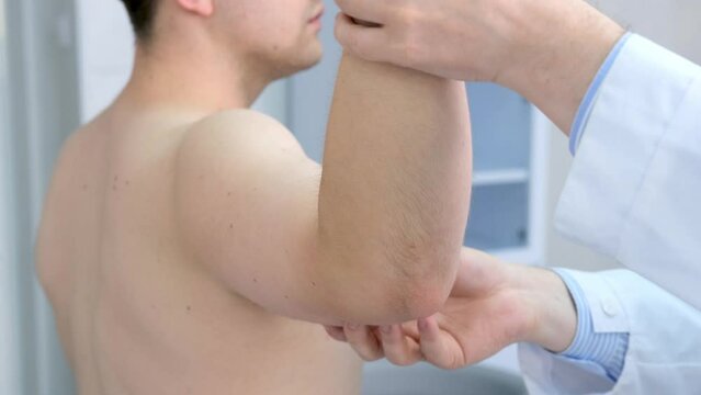 A male physiotherapist provides assistance to a male patient with an elbow injury, examines the patient in a rehabilitation center